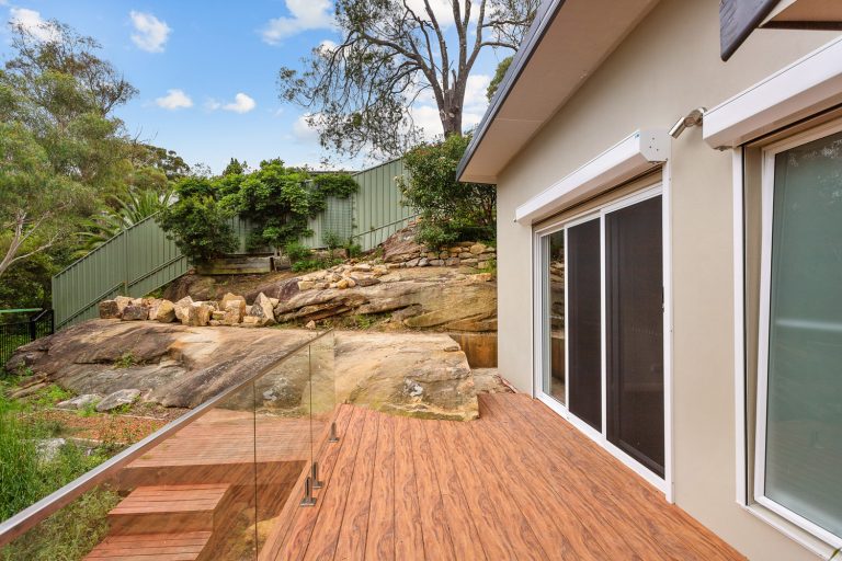 Finished deck beside the home, with glass balustrade and exposed sandstone
