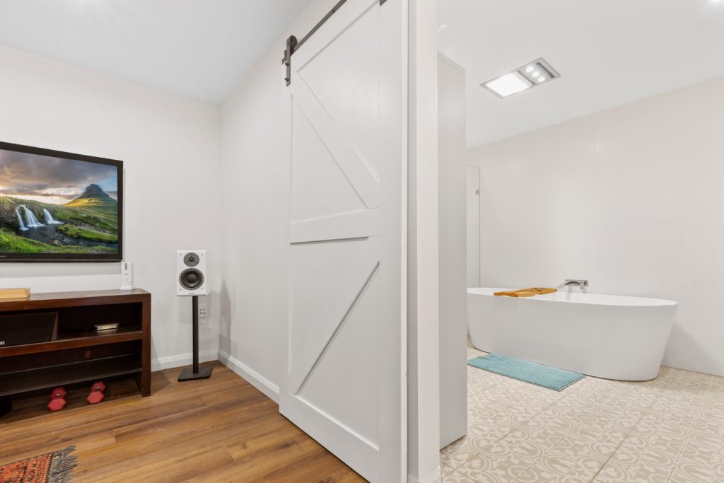 White sliding barn door connects the lower-level retreat to the bathroom with a freestanding bath.