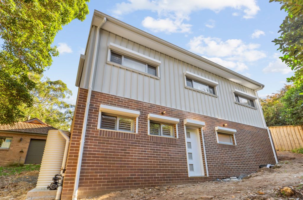 Rear elevation of the two-storey extension, with brick lower walls, vertical upper cladding and windows beneath external shutter housings.