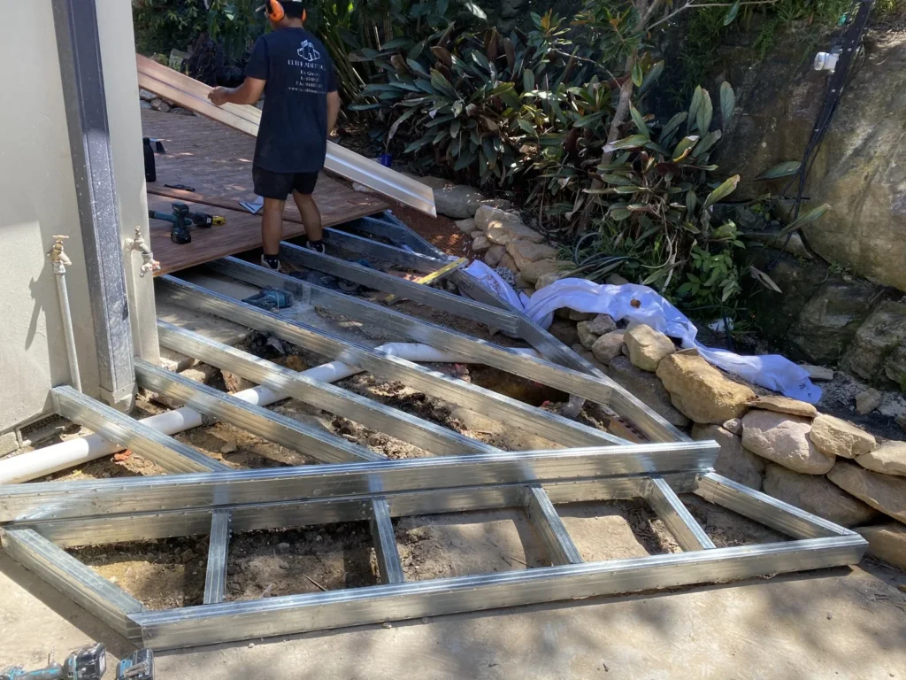 Metal deck framing follows the edge of the rock garden beside the house
